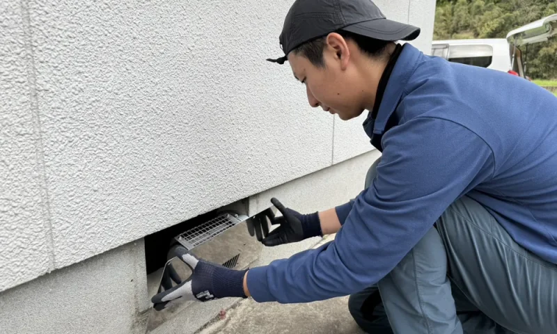 南日本消毒のスタッフが住宅外周の床下通気口を確認している様子