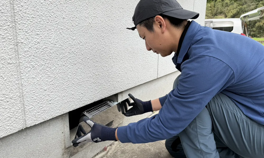 南日本消毒のスタッフが住宅外周の床下通気口を確認している様子