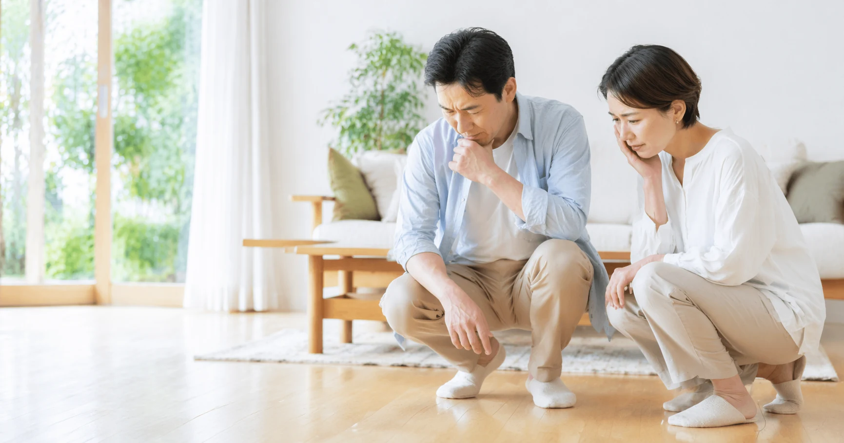 シロアリ被害が気になり、リビングで床付近を確認しながら相談する夫婦のイメージ
